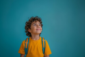 Portrait of happy latin schoolboy with backpack looking up at the sky, isolated on blue background. Back to school concept. Copy space.