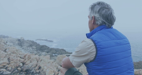 Wall Mural - Caucasian man gazes at the sea from a rocky shore, with copy space