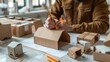 © BOONJUNG - Creative Designer Sketching Packaging Concept on Brown Cardboard with Mockup Box in Background