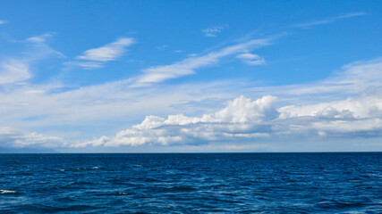 Wall Mural - View of the blue sea and white clouds above the horizon. View of small waves on the sea surface and thick white cumulus clouds in the blue sky above the horizon.