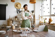© sofiko14 - Portrait of mature bearded male potter, standing in front of table with tools for sculpture. Positive male resting before making ceramic dishes from clay on background of shelves with tableware.