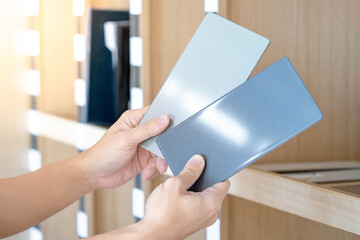 Wall Mural - Designer hands compare two gray laminate sheets near a wooden shelf in the material library. Choosing color board from collection for interior architecture and furniture finishing design