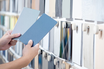 Wall Mural - Designer hands compare two gray laminate sheets nearby material swatch wall display in material library. Choosing color board from collection for interior architecture and furniture finishing design