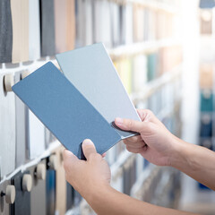 Wall Mural - Designer hands compare two gray laminate sheets nearby material swatch wall display in material library. Choosing color board from collection for interior architecture and furniture finishing design
