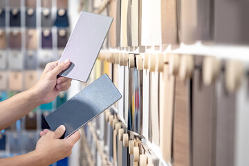 Wall Mural - Designer hands compare two gray laminate sheets nearby material swatch wall display in material library. Choosing color board from collection for interior architecture and furniture finishing design