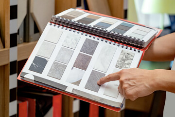 Wall Mural - designer hand pointing at sample stone material texture on furniture finishing catalog in material l
