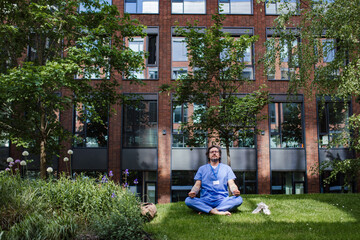 Doctor sitting on grass, meditating and relaxing, winding down from busy workday in hospital. Mental health and life balance for a healthcare worker.