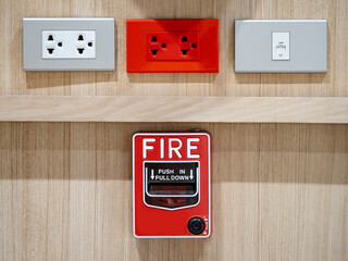 Emergency fire warning system pull station. Red fire alarm mounted on wooden wall near electrical power socket and telephone socket in public building