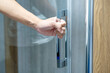 © Summer Paradive - Customer hand holding chrome door handle opening transparent glass door of modern shower room in home design store. Sanitary ware for bathroom interior design