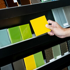 Wall Mural - Architect hand choosing and picking yellow lacquered glass tile on material samples shelf display in the material library. Colorful acrylic sheet collection for interior finishing idea