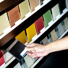 Wall Mural - Architect hand choosing and picking black lacquered glass tile on material samples shelf display in the material library. Colorful acrylic sheet collection for interior finishing idea