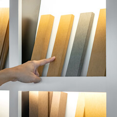 Wall Mural - designer hand choosing and picking wood plank or wooden lumber from display shelf in material librar