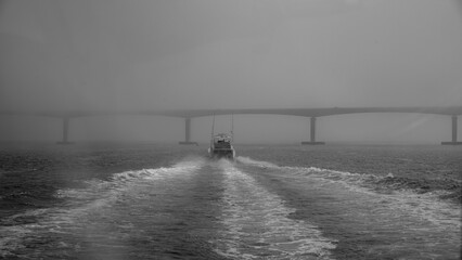 a boat traveling through the ocean under a bridge on a foggy day