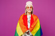 © ViDi Studio - Young smiling cheerful happy lesbian woman wear pink clothes wrapped in striped rainbow flag look camera isolated on plain purple background studio portrait. Pride day June month love LGBTQ concept.