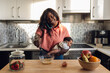 © Westend61 - Mature woman talking on phone and holding baby girl in kitchen