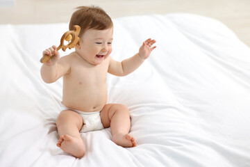 Canvas Print - Happy baby boy with wooden rattle on bed at home. Space for text