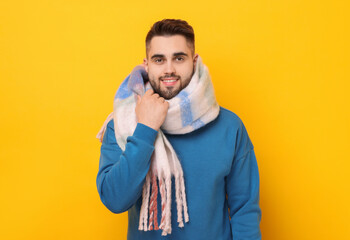 Wall Mural - Smiling man in warm scarf on yellow background