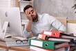 © New Africa - Overwhelmed man sitting at table with computer and stack of folders in office