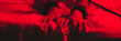 © alexkoral - hands in BDSM handcuffs of a submissive female slave on a sheet on a bed with a red light. Wide horizontal banner header