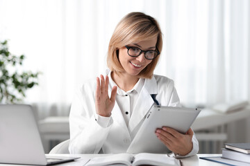 Canvas Print - Smiling doctor with tablet having online consultation at table in office