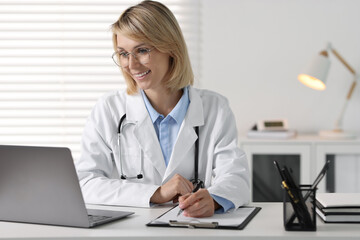 Wall Mural - Smiling doctor with laptop having online consultation at table in office