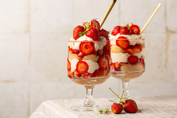 Strawberry tiramisu or trifle in two glasses. Italian dessert on a light table and white tile background. Copy space.