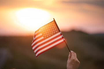 Wall Mural - Woman`s hand holding a waving american USA flag in magic sunset.