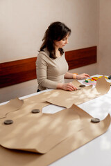 professional seamstress works with kraft paper to draw future patterns for a dress