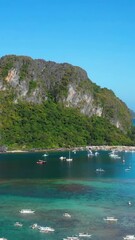 Wall Mural - Boats anchored over corals near cliffs in El Nido Philippines vertical video.