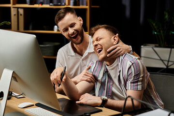 Wall Mural - Two men, in casual attire, sit together in front of a computer working.