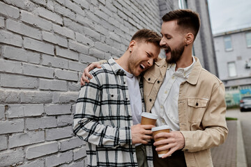 Two men in casual attire standing together by a brick wall.