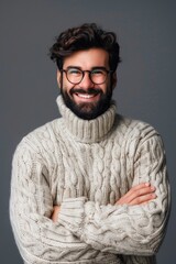 Wall Mural - A man with glasses and a beard is smiling and wearing a white sweater. He is posing for a picture and has his arms crossed