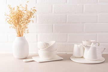 Wall Mural - A set of white ceramic tableware for a tea ceremony, a vase with ears of wheat on a stylish countertop. a white brick wall. Cozy bright kitchen.