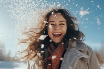 Wall Mural - A woman with long hair is smiling and blowing snow. She is wearing a scarf and a coat