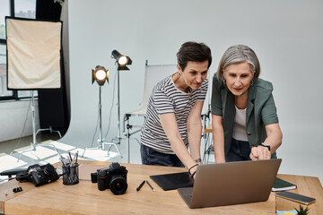 Two middle-aged women, work together on a laptop in a professional modern photo studio.