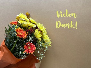 Thank you or Vielen Dank in German, Floral Bouqet with Yellow and Orange Flowers on Brown Background.