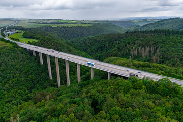 Wall Mural - cargo trucks on the highway on the bridge. asphalt road among green forest and beautiful rain clouds. cargo delivery and transportation concept