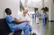 © Maskot - Happy senior doctor discussing with colleague while sitting in corridor of hospital