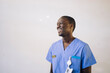 © Maskot - Happy male doctor in blue scrubs standing in front of white wall