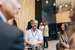 © Maskot - Happy mature businessman with disability sitting on wheelchair while discussing with delegates at convention center