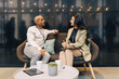 © Maskot - Businessman listening to female entrepreneur discussing strategies while sitting on couch at convention center