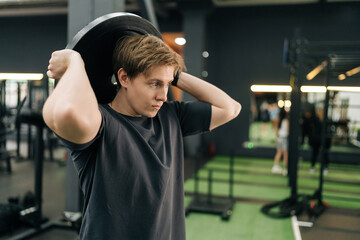 Dedicated beginner sportsman in activewear holding and rotating weight disc plate overhead during sport workout training in modern gym. Concept of healthy lifestyle, physical sport activity.