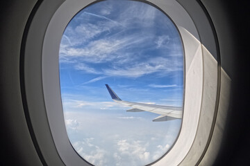 View of airplane wings in clouds through porthole. Blue sky background. Beautiful clouds and airplane wings from the window with beautiful blue sky