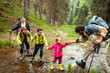 © Marko Geber - Multi-generational family crossing a stream during a forest hike
