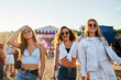 © artiemedvedev - Girls enjoy summer music festival on sandy beach at sunset. Three friends dance, laugh near stage with bright lights. Fashionable young women in casual outfits fun, celebrate during outdoor concert.
