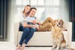 © BillionPhotos.com - happy couple sitting together on sofa with a dog