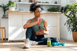 © nenetus - Athletic woman eating a healthy fruit bowl while sitting on floor in the kitchen at home
