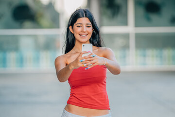 smiling girl in summer clothes on the street taking photo with mobile phone