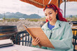 © EdNurg - A young woman smiles while reading the menu at a lakeside restaurant, enjoying the panoramic view of lake as she contemplates her dining choices.
