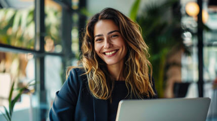 Wall Mural - Portrait of a young woman sitting with a laptop in a modern office. Smiling woman working with a laptop computer. Freelancing concept. Lifestyle.